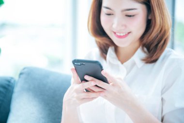 Akıllı telefon kullanan Asyalı bir kadın online sosyal medya alışveriş sitesini akıllı telefondan gülümseyen yüzüyle kullanıyor. Cep telefonu tutan Asyalı kadının mutluluğu e-postaları kontrol ediyor Blog sosyal medya bloğu okuyor