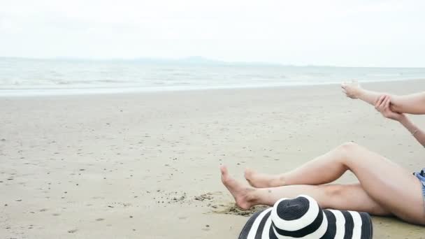 夏の女性ビキニは ビーチで日焼け止めローションSpfサンブロックを使用しています 陽気な女性は 白いビキニ 短いパンツ ビーチで日焼け止めと熱帯の島に座っているわら帽子を着用海を見て — ストック動画