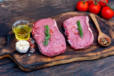 Biberiye, tuz, sarımsak, domates, karabiber ve zeytinyağı ile ahşap masa arkasında çiğ et bifteği taze organik malzeme. Biftek ve çiğ et için ahşap tabakta et.