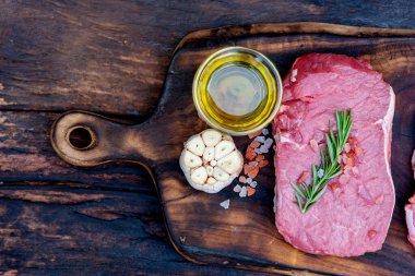 Biberiye, tuz, sarımsak, domates, karabiber ve zeytinyağı ile ahşap masa arkasında çiğ et bifteği taze organik malzeme. Biftek ve çiğ et için ahşap tabakta et.
