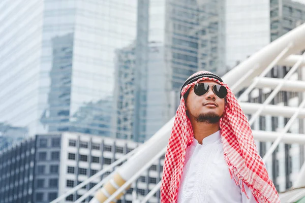 Handsome modern Arabian man standing in modern city wear muslim dress headscarf eastern ethnic smile outside office. Arab Man looking plan new project while walking in big city. Business successful
