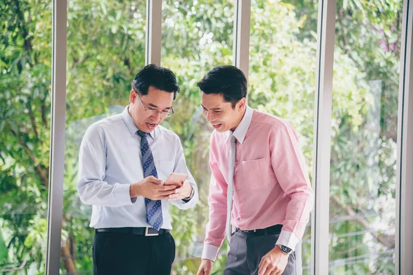 Success Businessman happy got good news from mobile smart phone that business so success. Asian young business man raise hand with happiness, smiling, excited after got great news from phone.