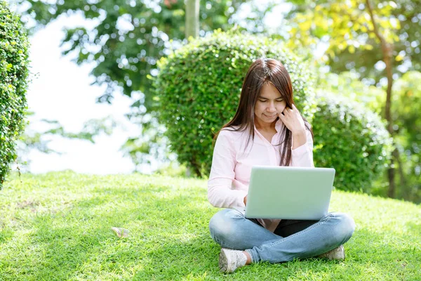 Asian woman sitting green park using laptop computer. Woman working on laptop happy entrepreneur business using notebook with hands typing on keyboard home office during coronavirus quarantine period