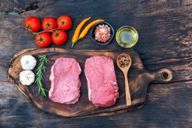 Biberiye, tuz, sarımsak, domates, karabiber ve zeytinyağı ile ahşap masa arkasında çiğ et bifteği taze organik malzeme. Biftek ve çiğ et için ahşap tabakta et.