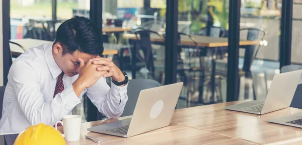 Asian young engineer man stress and failure in architecture project sitting at office on construction site. Upset despair civil construction engineer working on laptop with stressed problems