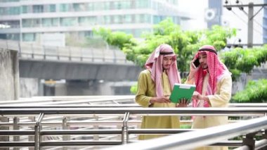Müslüman modern uae şehrinde akıllı telefon uygulaması ve iş belgeleri klasörü kullanan İslami bir adam. Arap erkekler başörtüsü takıyor ve Müslüman resmi giysileri iş dünyasında tartışıyorlar