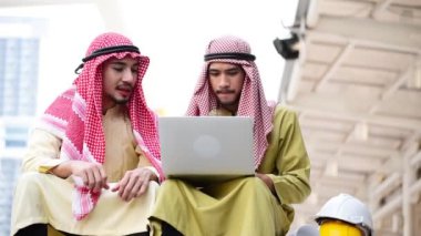 İslami adam, modern müslüman uae şehrinde dizüstü bilgisayar ve iş belgesi kullanıyor. Arap erkekleri tesettür ve Müslüman resmi giysileri giyer iş görüşmesinde tartışırlar