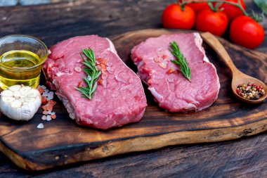 Biberiye, tuz, sarımsak, domates, karabiber ve zeytinyağı ile ahşap masa arkasında çiğ et bifteği taze organik malzeme. Biftek ve çiğ et için ahşap tabakta et.