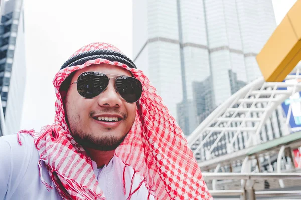 Handsome modern Arabian man standing in modern city wear muslim dress headscarf eastern ethnic smile outside office. Arab Man looking plan new project while walking in big city. Business successful