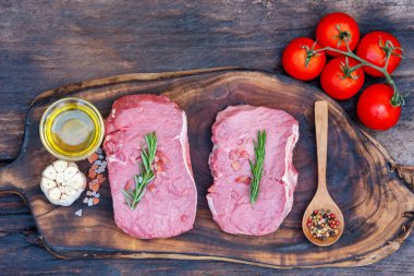 Biberiye, tuz, sarımsak, domates, karabiber ve zeytinyağı ile ahşap masa arkasında çiğ et bifteği taze organik malzeme. Biftek ve çiğ et için ahşap tabakta et.