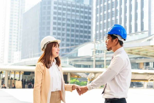 Civil Construction engineer teams shaking hands together wear work helmets worker on construction site. Foreman industry project working engineer teamwork. Two asian engineer team shake hands together