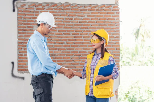 Civil Construction engineer teams shaking hands together wear work helmets worker on construction site. Foreman industry project working engineer teamwork. Two asian engineer team shake hands together