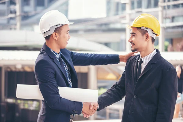 Civil Construction engineer teams shaking hands together wear work helmets worker on construction site. Foreman industry project working engineer teamwork. Two asian engineer team shake hands together
