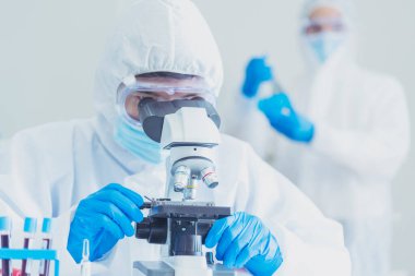 Erkek bilim adamı bilim laboratuarındaki mikroskop araştırmalarına bakar. Asyalı bilim adamı laboratuvar kimya laboratuvarlarını arıyor. Covid-19 Coronavirus biyokimya araştırma deneyi aşı konsepti