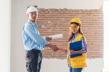 İnşaat mühendisi takımları el sıkışırken inşaat alanında kask takıyor. Foreman Endüstri Projesi Mühendis ekip çalışması. İki Asyalı mühendis takımı el sıkışıyor.