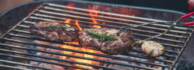 Banner BBQ Barbekü ızgara et çubuğu ateşte kızartılıyor, dışarıda kömür pişiriliyor. Banner Beef ızgara piknik pirzolası domuz pastırması Amerikan mutfağı. Izgara domuz eti, bbq raf alevi ve fotokopi alanı