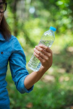 Dikey Genç Kadın Su İçen Şişe Açık Park Gezgini. Asyalı kadın içme suyu şişesi sağlıklı ve mutlu bir insan. Dikey görüntüler. Mineral içeceği şişesi tutan güzel Asyalı kadınlar.