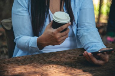 Yeşil Park 'ta kahve içen bir kadın elinde sıcak tek kullanımlık bardak tutuyor. Happy rahatla güzel Asyalı kadın gülümseyen yüz açık hava bahçesinde duruyor. Genç kadınlar doğanın tadını çıkarıyorlar Özgürlük yaşam tarzı.