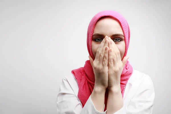 Indoor head shot of optimistic Muslim woman with surprising face expression closing her mouth with two hands. — Stock Photo, Image