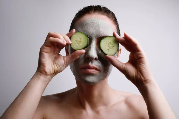 Retrato de mujer joven con una mascarilla en la celebración de un rodajas de pepino delante de un ojo. Concepto de belleza y cuidado de la piel . —  Fotos de Stock