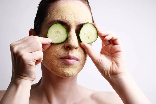 Retrato de mujer joven con una mascarilla en la celebración de un rodajas de pepino delante de un ojo. Concepto de belleza y cuidado de la piel . —  Fotos de Stock