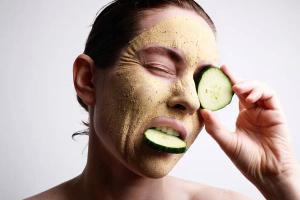 Egy maszkos nő, aki egy uborka szeletet tart az egyik szeme előtt. Szépség és bőr koncepció. — Stock Fotó