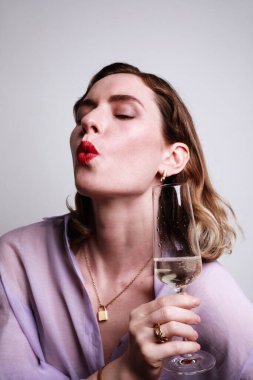 Parti zamanı. Mor gömlekli, şampanya içen çekici bir kadının dikey portresi. Stüdyo çekimi.