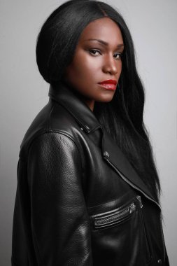 Gri duvarda poz veren motorcu ceketi giyen genç siyahi bir modelin dikey portresi. Stüdyo Çekimi.
