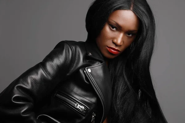 Headshot of young black female model, wearing biker jacket posing over grey wall. Studio Shot.