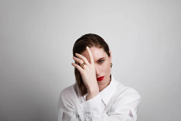 Attraktive junge Frau mit weißem Hemd und roten Lippen, die ihr Gesicht berührt und in die Kamera blickt. Kopierraum. — Stockfoto