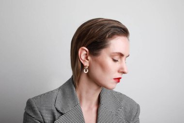 Ceketli ve kırmızı dudaklı çekici genç bir kadın, yan bakıyor ve güler yüzle gülümsüyor. Boşluğu kopyala.