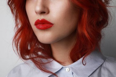 Uzun kızıl saçlı, parlak makyajlı, gri arkaplanda poz veren çekici bir genç kadının yakın plan portresi..