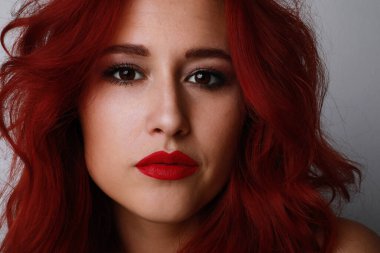 Uzun kızıl saçlı, parlak dudaklı çekici bir kadın stüdyoda poz veriyor. Kendine güvenen kadın..