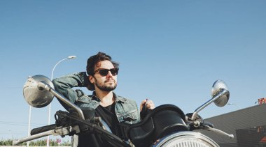 Sakallı mutlu motosikletçi elinde kaskla yolda duruyor..