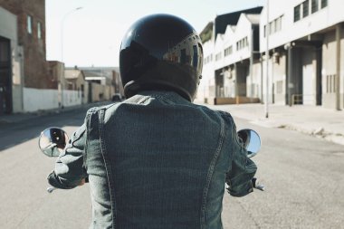 Motosikletlinin arka tarafında, siyah kasklı, büyük bir motosikletle yolda kalıyor..