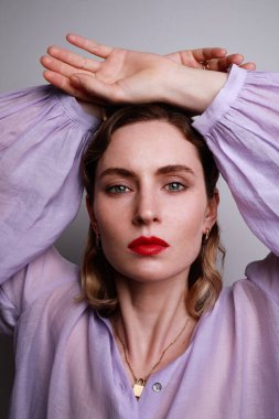 Mor gömlekli, elleri beyaz arka planda poz veren güzel bir kadının dikey yakın çekimi..