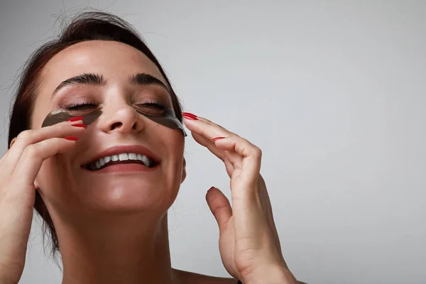 Optimista fiatal nő vigyáz a szem alatti bőrre. Bőrápolási koncepció. A szöveg helye. — Stock Fotó