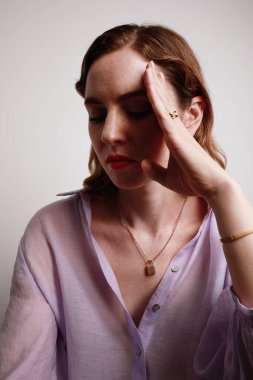 Mor gömlekli genç bir kadının dikey portresi. Beyaz arka planda el üstünde poz veriyor..