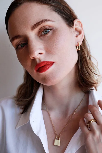 Kırmızı dudaklı güzel bir kadının dikey yakın plan portresi ve beyaz duvar arkasında duran altın mücevherler.. — Stok fotoğraf