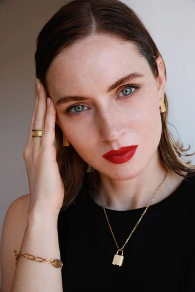 Close-up vertical de mulher atraente com lábios vermelhos e vestindo jóias douradas posando sobre fundo da parede branca. — Fotografia de Stock