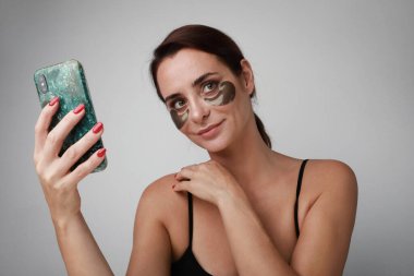 Gri arka planda yüzü güzellik ürünüyle gülümseyen güzel bir genç kadının portresi..