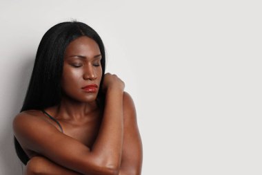 Kapalı gözlü, uzun saçlı, beyaz arka plan duvarında poz veren siyah kadının yakın plan portresi..