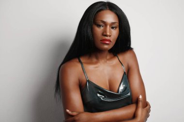 Siyah kadının portresi, uzun saçlı ve gece elbisesiyle, beyaz arka plan duvarında poz veriyor. Metin için boşluk.