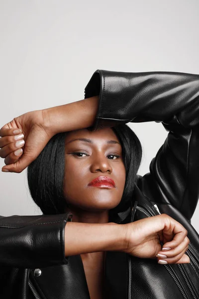 Retrato vertical close-up da jovem mulher negra bonita vestindo uma jaqueta de couro contra a parede branca. — Fotografia de Stock