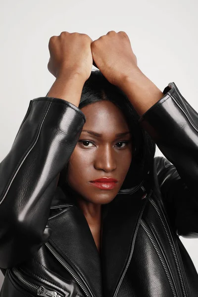 Gambar close-up vertikal dari wanita muda berkulit hitam yang menarik mengenakan jaket kulit menghadap dinding putih. — Stok Foto