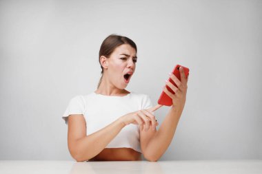 Güzel, beyaz bir kadın akıllı telefon kullanıyor. Şaşırmış bir yüzle korkmuş ve korku ifadesinden heyecanlanmış.