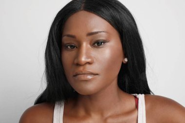 Beyaz duvarın üzerinden izole edilmiş kameraya bakan genç siyahi kadının yakın plan portresi..