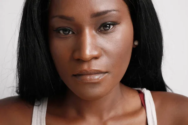 Close-up retrato de mulher negra com expressão facial séria, posando na parede de fundo branco. — Fotografia de Stock
