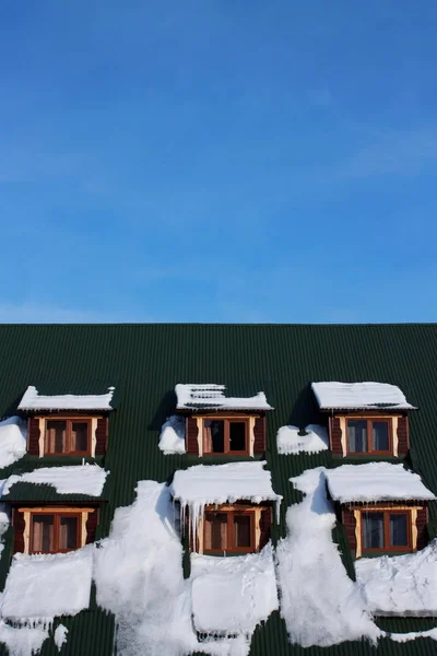Green roof of the house with snow against on blue sky