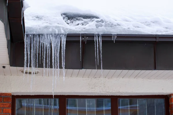 Sharp icicles and melted snow hanging from eaves of roof